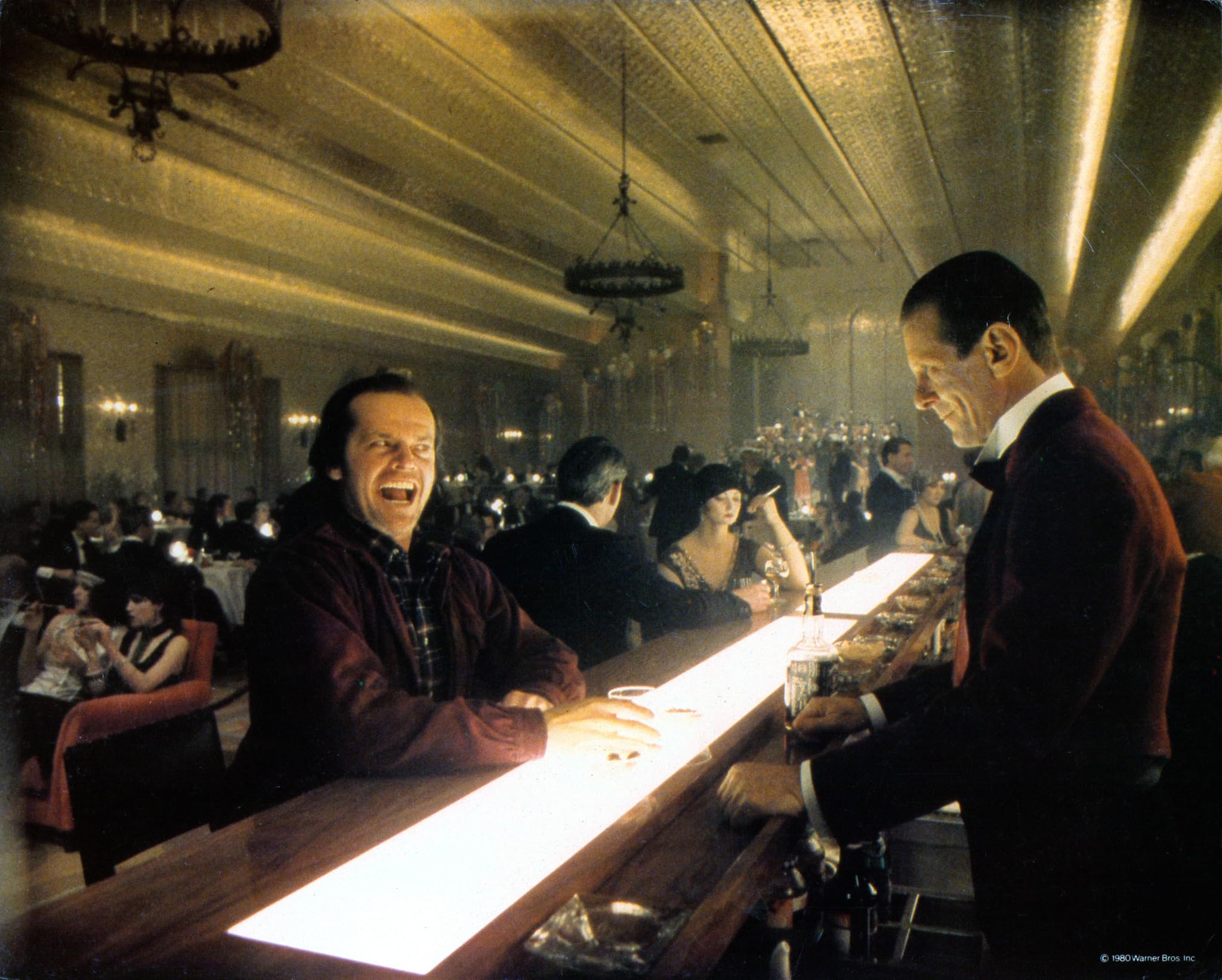 Jack laughs at the bar while Lloyd watches him, setting up the hotel's seductive menace.